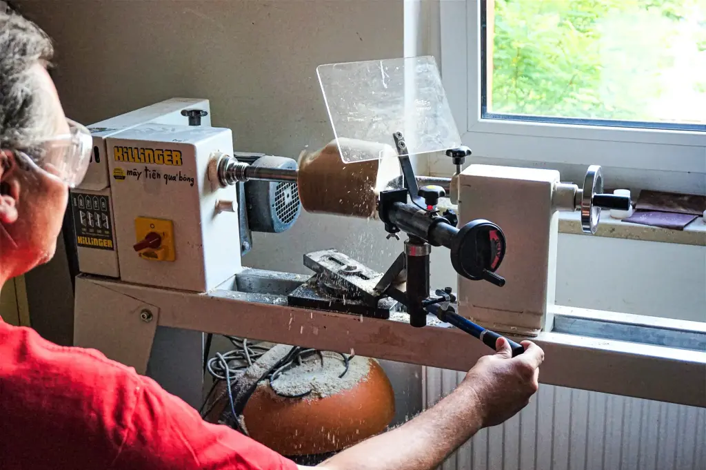 Ein Mann bedient eine Drehmaschine, um ein Stück Holz zu formen und seine handwerklichen Fähigkeiten zu demonstrieren. Beispielprojekt Soziale Projekte von Revonner. Trotz Einschränkungen können die Teilnehmer der Werkstatt nun an der Drehbank arbeiten.
