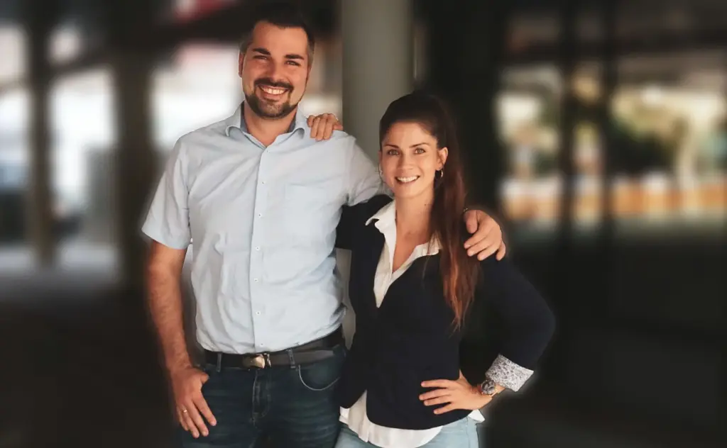 Zwei Personen, eine Frau und ein Mann stehen nebeneinander, sie lächeln beide, sie sind das Gründerpaar von Revoneer Produktentwicklung in München, Victoria und Dominik Blendl.